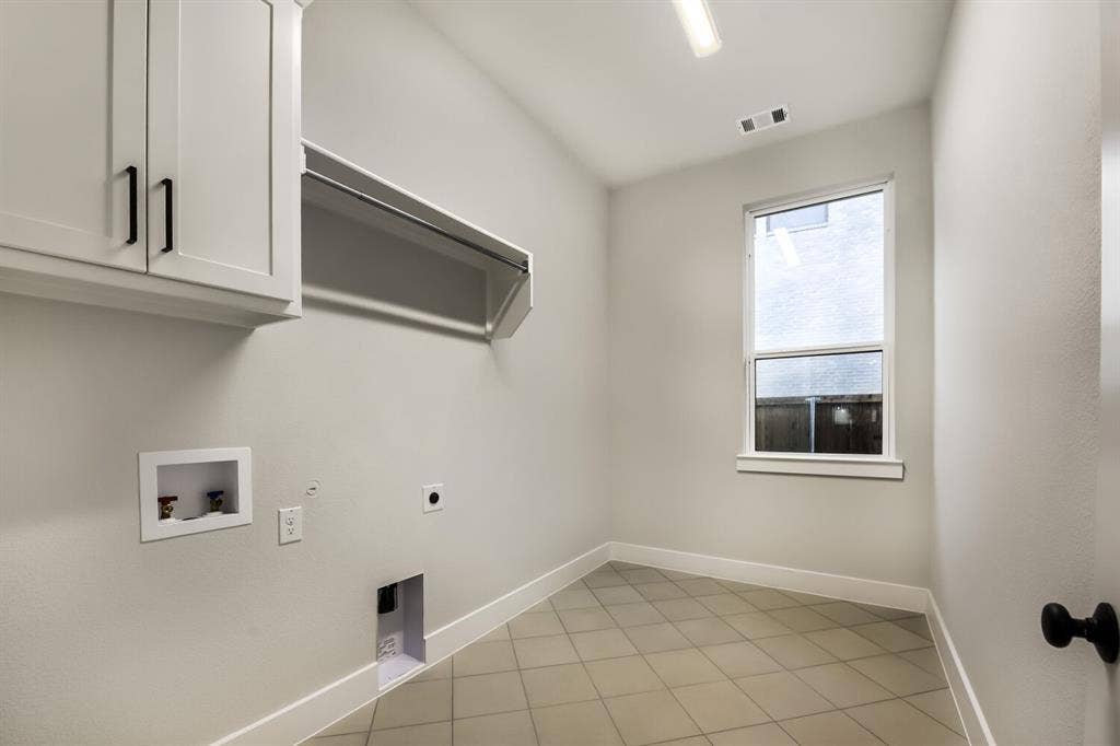 Dedicated utility room featuring light-toned tiled flooring, white shaker-style cabinetry with black hardware, a built-in hanging rod, and a window for natural light