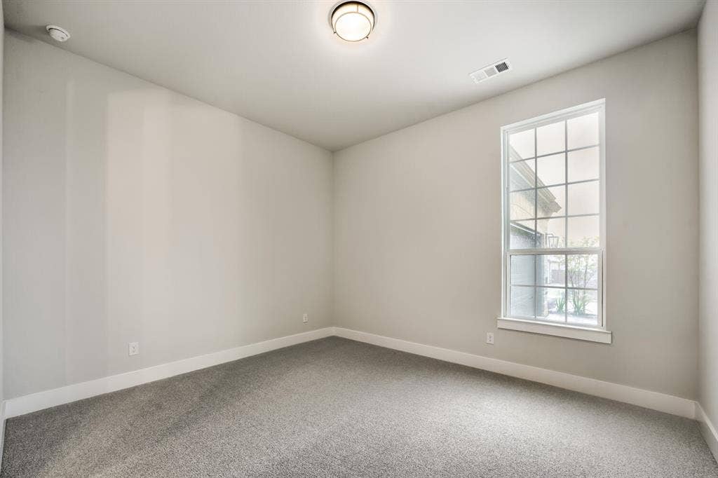 Neutral-toned room featuring a large window with grid panes, grey carpet flooring, white baseboards, and a flush-mount ceiling light