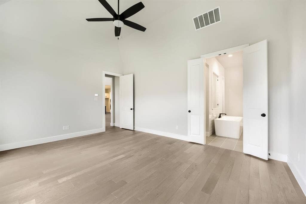 Spacious room featuring vaulted ceilings, a contemporary black ceiling fan, and light wood-finish flooring