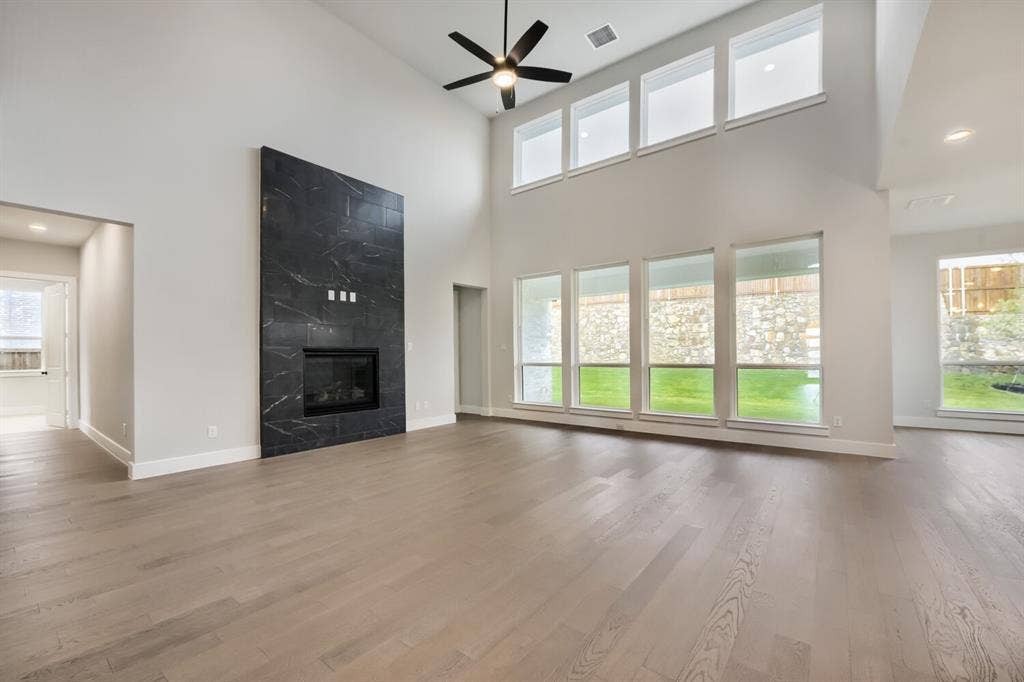 Vaulted ceiling with an integrated ceiling fan, a floor-to-ceiling fireplace featuring dark stone tiling, wood-finish flooring, and multiple large windows