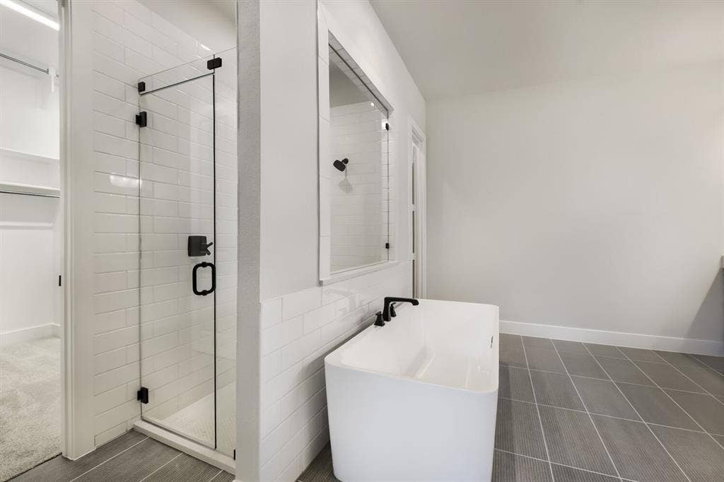 Freestanding soaking tub with matte black fixtures, glass-enclosed shower with subway tile surround, patterned floor tiling, and a recessed mirror
