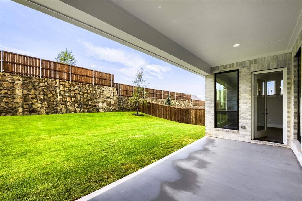 Covered concrete patio with recessed lighting, light-colored brick exterior, and large black-framed windows