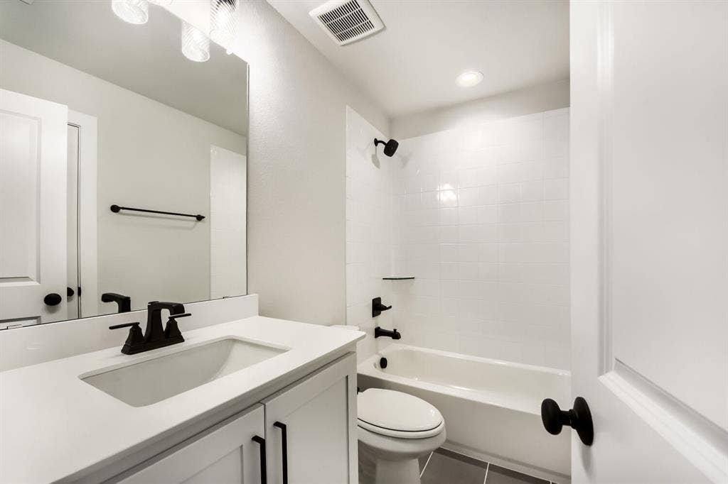 Full bathroom featuring a white vanity with integrated sink, black fixtures, and a coordinating white bathtub with subway tile surround