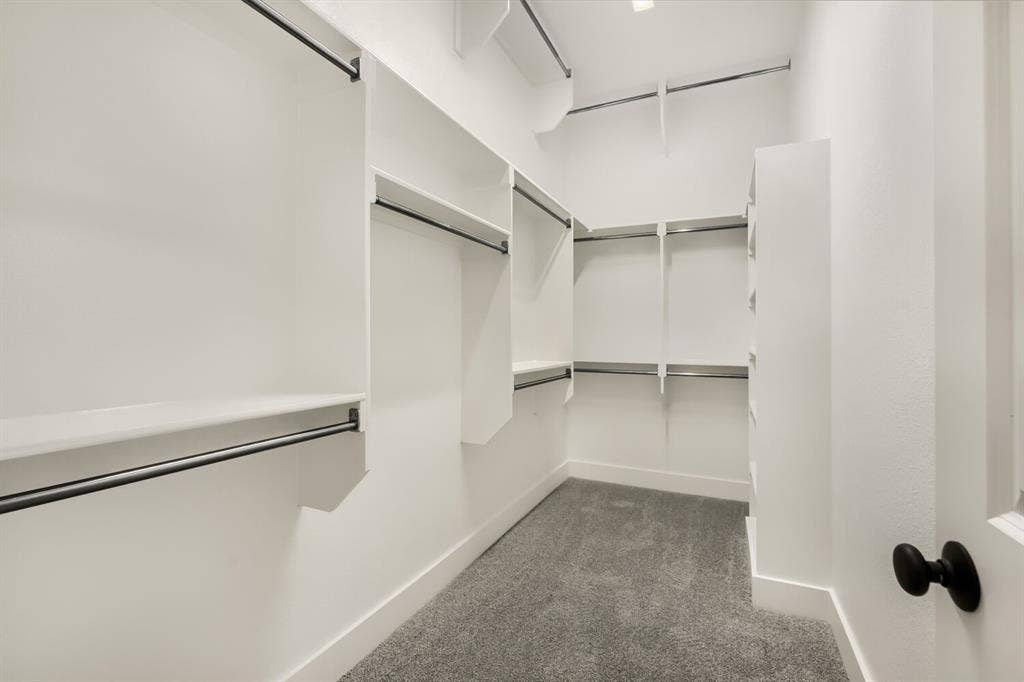 Expansive walk-in closet featuring built-in shelving, multiple hanging rods, recessed lighting, and soft gray carpeting