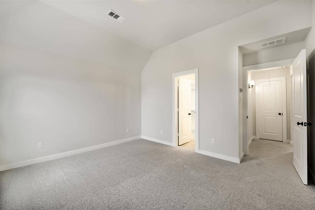 Spacious room featuring light gray carpeting, neutral wall paint, white baseboards, and a vaulted ceiling