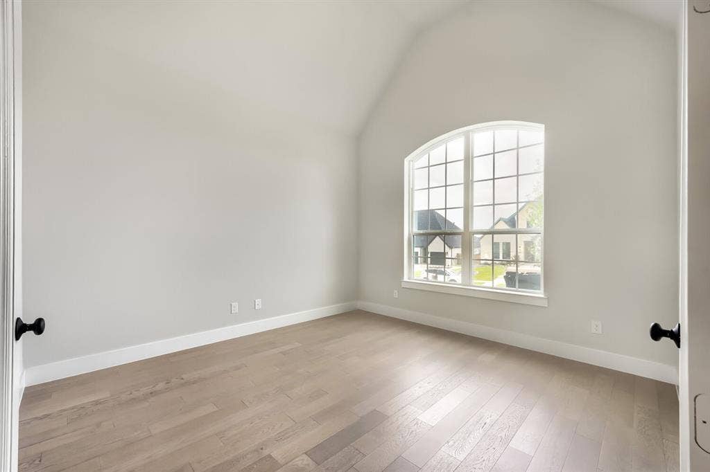 Room with vaulted ceiling, arched window, and wood-finish flooring