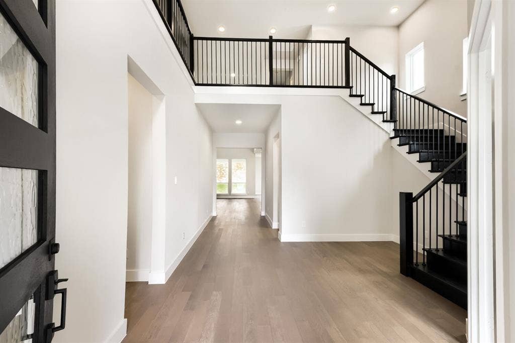 Two-story foyer featuring a contemporary black wood-finish and metal staircase, wood-finish flooring, recessed lighting, and a modern entryway door with textured glass panels