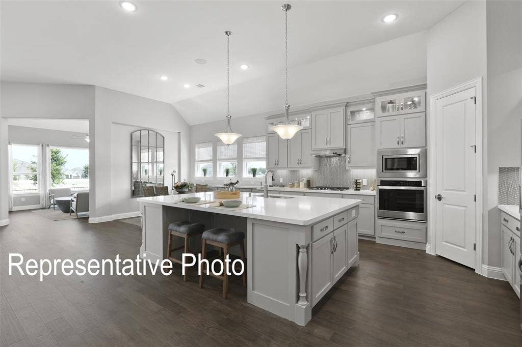 4384 Laurel Trail, Midlothian, TX 76065 Gourmet kitchen featuring a substantial island with seating, pendant lighting, stainless steel appliances, custom cabinetry, and wood-finish flooring