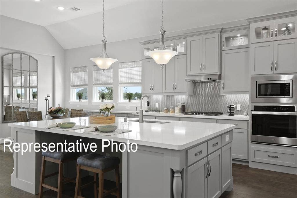 4384 Laurel Trail, Midlothian, TX 76065 Gourmet kitchen featuring a spacious island, light gray cabinetry, stainless steel appliances, a herringbone tile backsplash, and wood-finish flooring