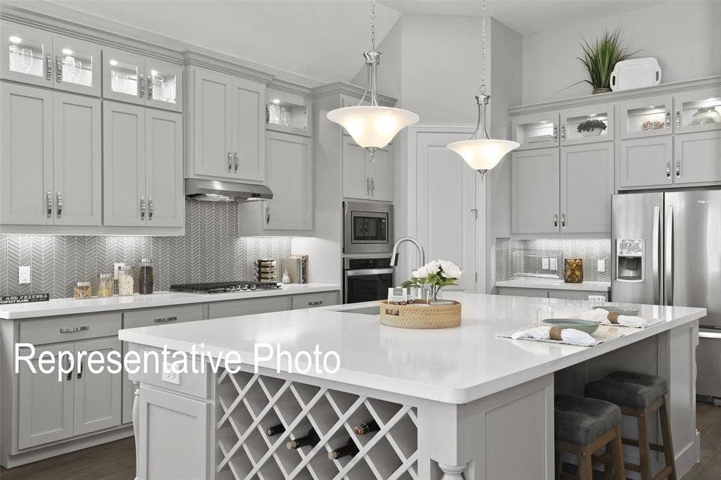 4384 Laurel Trail, Midlothian, TX 76065 Kitchen featuring light gray cabinetry, stainless steel appliances, a chevron-patterned tile backsplash, and a central island with an integrated wine rack