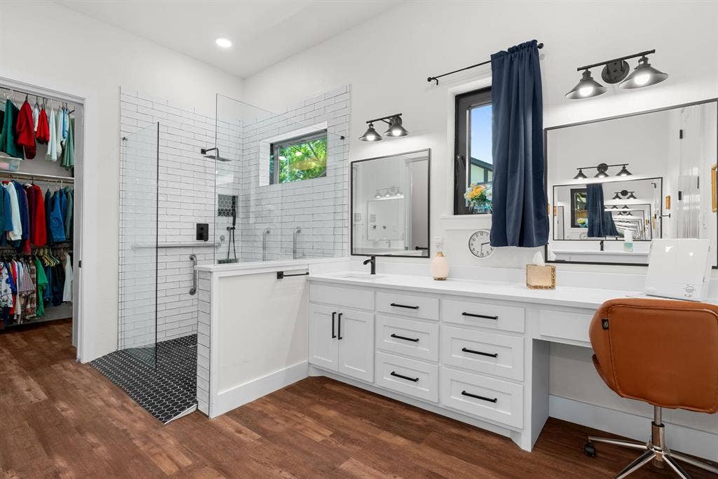 3621 Fritz Lane, Corinth, TX 76208 Spacious bathroom featuring a glass-enclosed shower with white subway tile, an expansive double vanity with white cabinetry and dark hardware, wood-finish flooring, and a walk-in closet