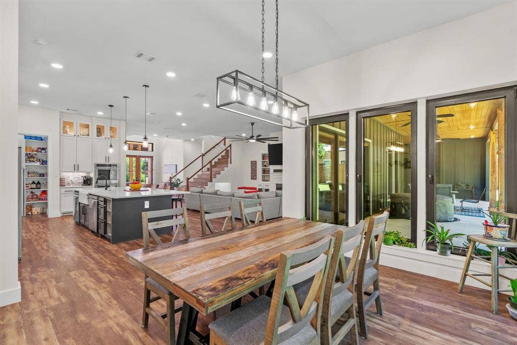3621 Fritz Lane, Corinth, TX 76208 Open-concept interior featuring wood-finish flooring throughout, a modern kitchen with a large island, a dining area with a linear chandelier, and sliding glass doors opening to an outdoor patio