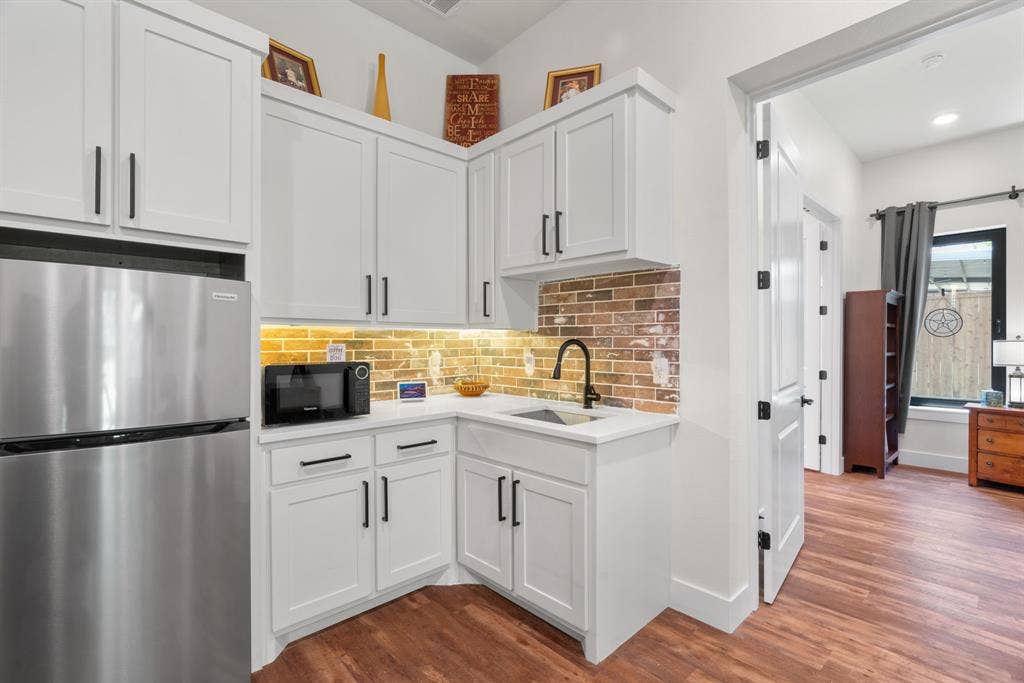 3621 Fritz Lane, Corinth, TX 76208 Compact kitchen area featuring white shaker cabinetry, stainless steel appliances, and a brick-patterned backsplash