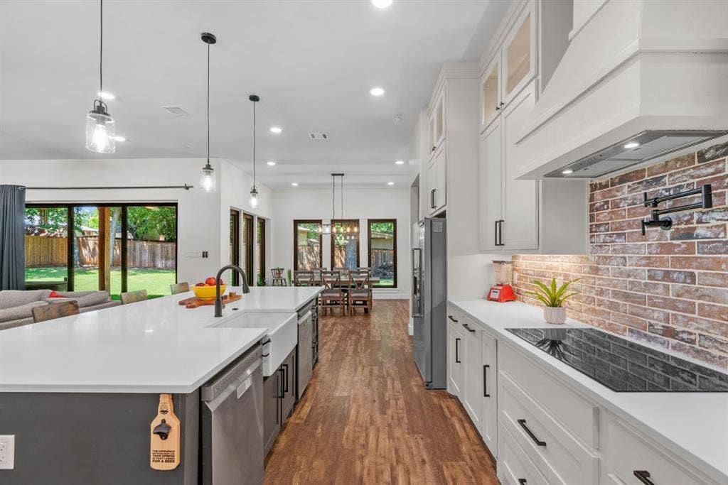 3621 Fritz Lane, Corinth, TX 76208 Gourmet kitchen featuring a large central island with a farmhouse sink, stainless steel appliances, a brick-finish backsplash, white cabinetry, and wood-finish flooring