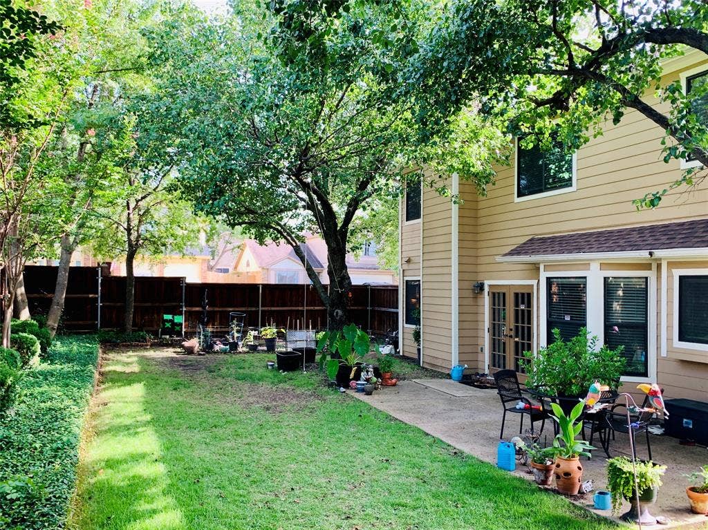 1848 Sonnet Drive, Grapevine, TX 76051 Expansive backyard featuring a concrete patio area, mature trees, manicured hedges, a privacy fence, and multiple window openings with blinds