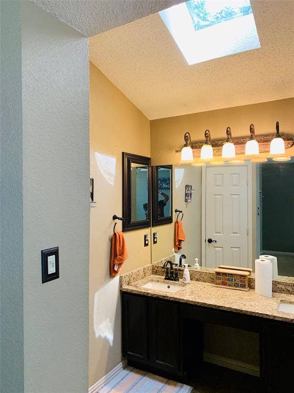 1848 Sonnet Drive, Grapevine, TX 76051 Vaulted ceiling with skylight, dual vanity with granite-finish countertop, dark wood-finish cabinetry, and contemporary light fixture
