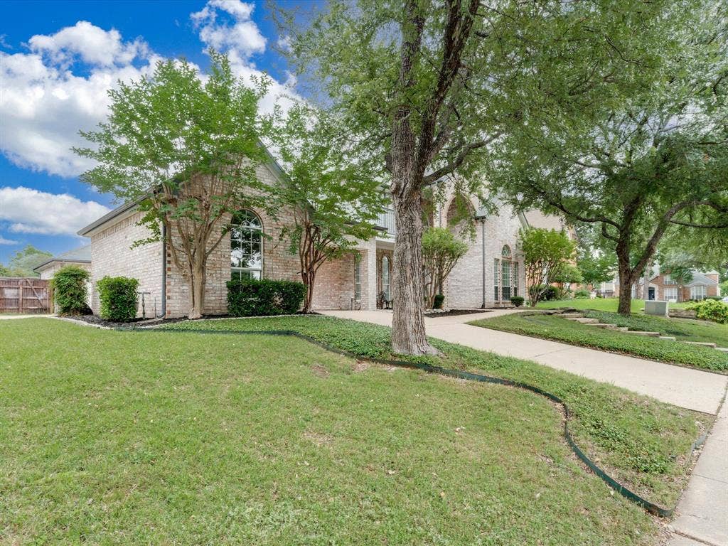 736 Sunkist Lane, Plano, TX 75025 Brick exterior with arched window, concrete driveway, mature trees, and landscaped garden beds