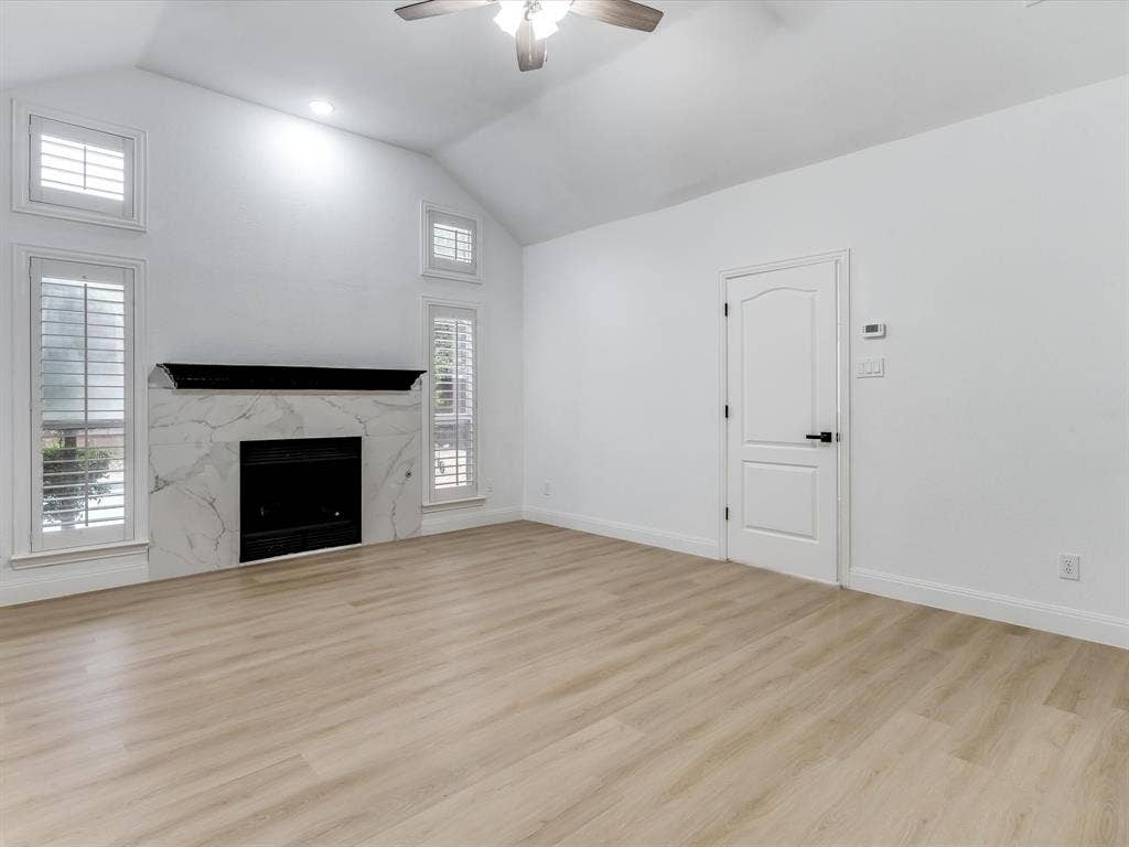 736 Sunkist Lane, Plano, TX 75025 Spacious room featuring vaulted ceilings, a central fireplace with a marble-finish surround, wood-finish flooring, and white plantation shutters on multiple windows