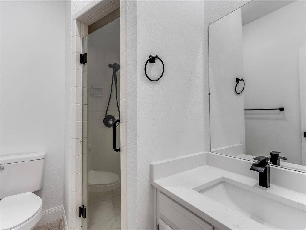 736 Sunkist Lane, Plano, TX 75025 Contemporary bathroom featuring a frameless glass shower enclosure with matte black hardware, a shower head with an attached sprayer, a white vanity with an integrated sink, a quartz countertop, and a matte black faucet