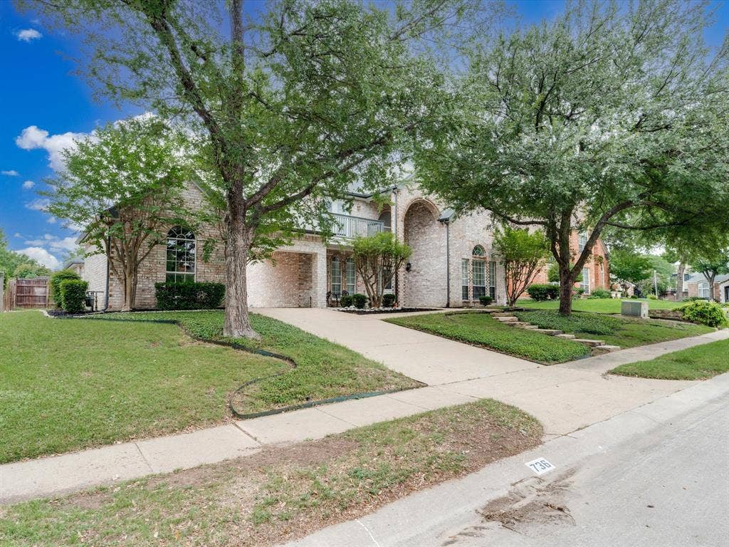 736 Sunkist Lane, Plano, TX 75025 Traditional brick exterior featuring a covered entry, arched window accents, mature trees, and a concrete driveway