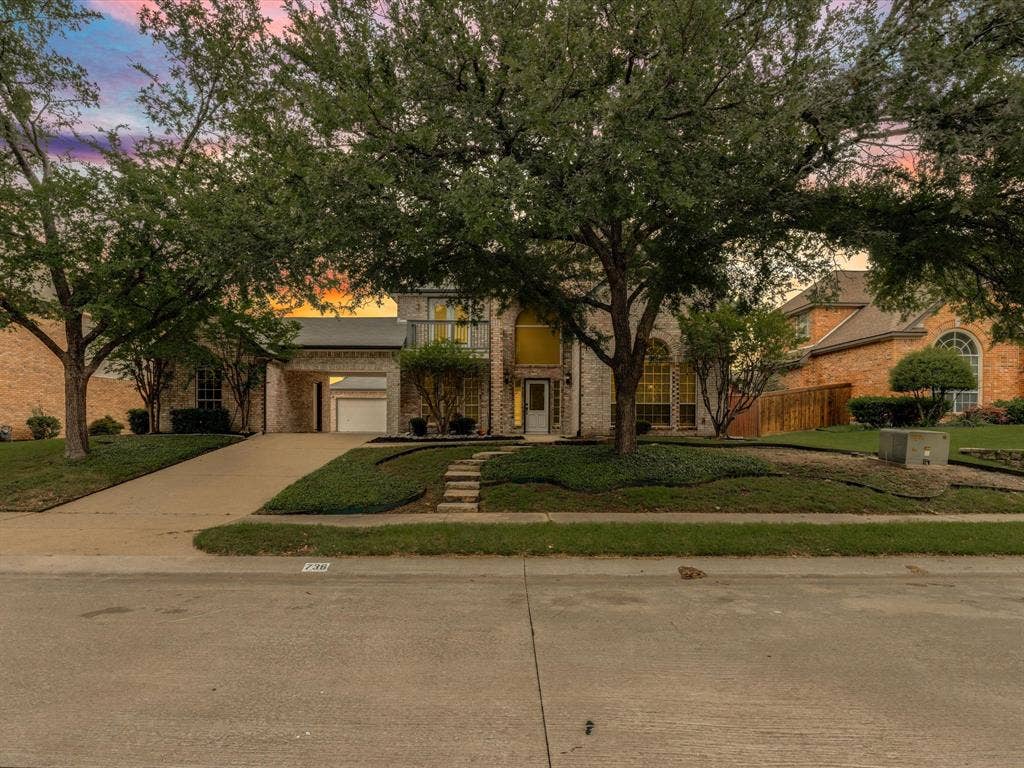 736 Sunkist Lane, Plano, TX 75025 Two-story brick facade property featuring an arched entry, mature front yard trees, a concrete driveway, and built-in landscaping