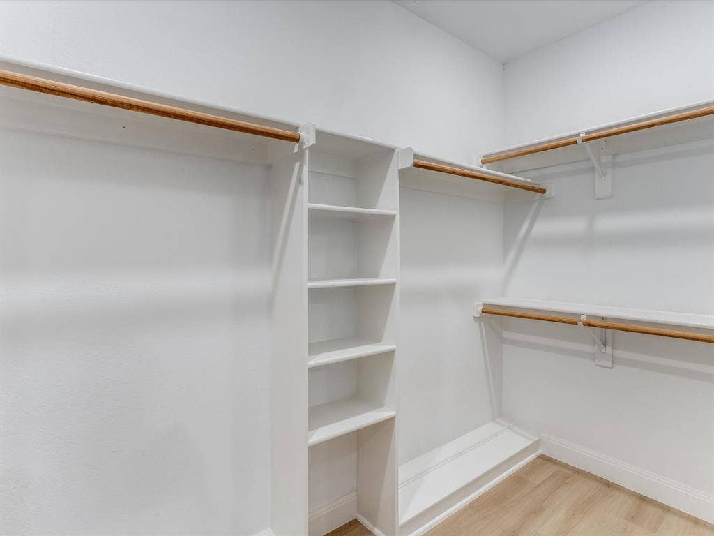 736 Sunkist Lane, Plano, TX 75025 Walk-in closet featuring built-in shelving, multiple hanging rods, white trim, and wood-finish flooring