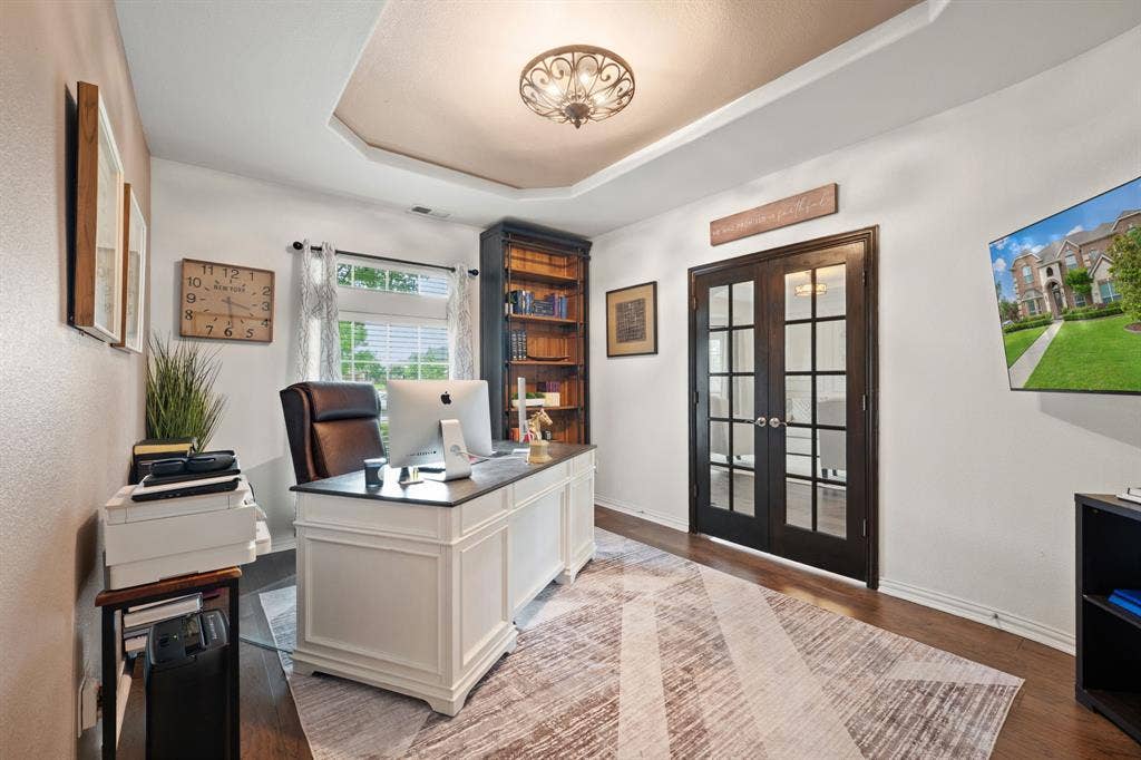 Office space featuring a tray ceiling with decorative lighting, wood-finish flooring, and French pane double doors