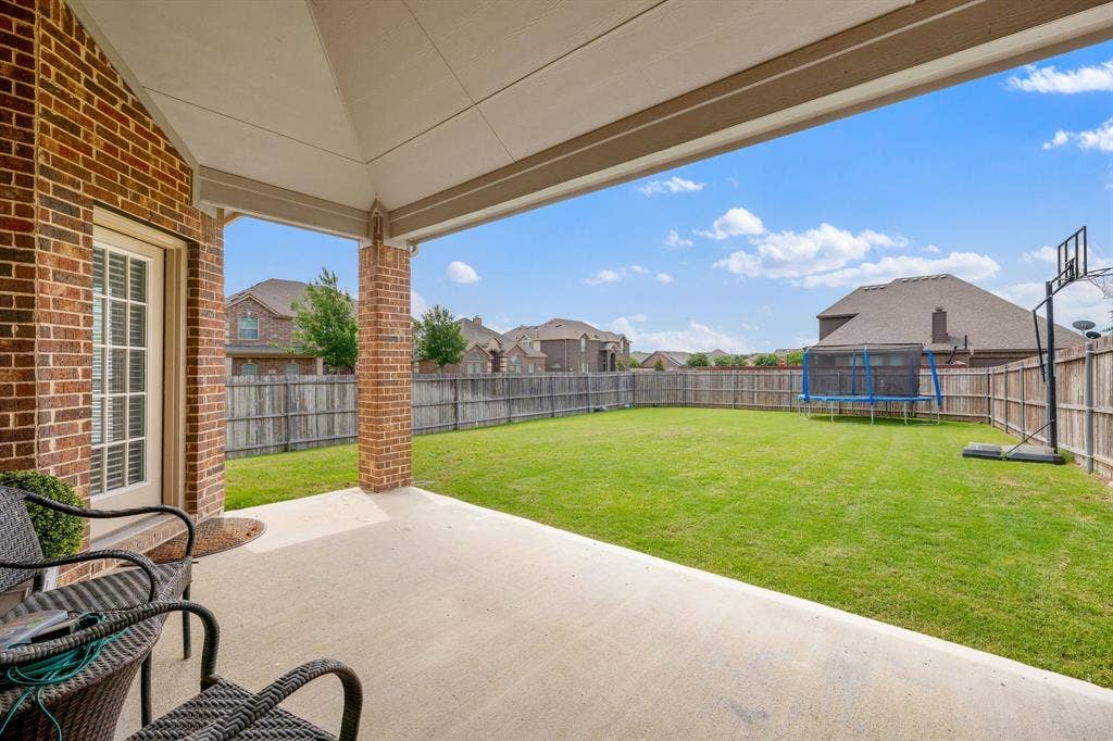 Covered patio with brick columns and a concrete surface, opening to a spacious fenced backyard with a green lawn