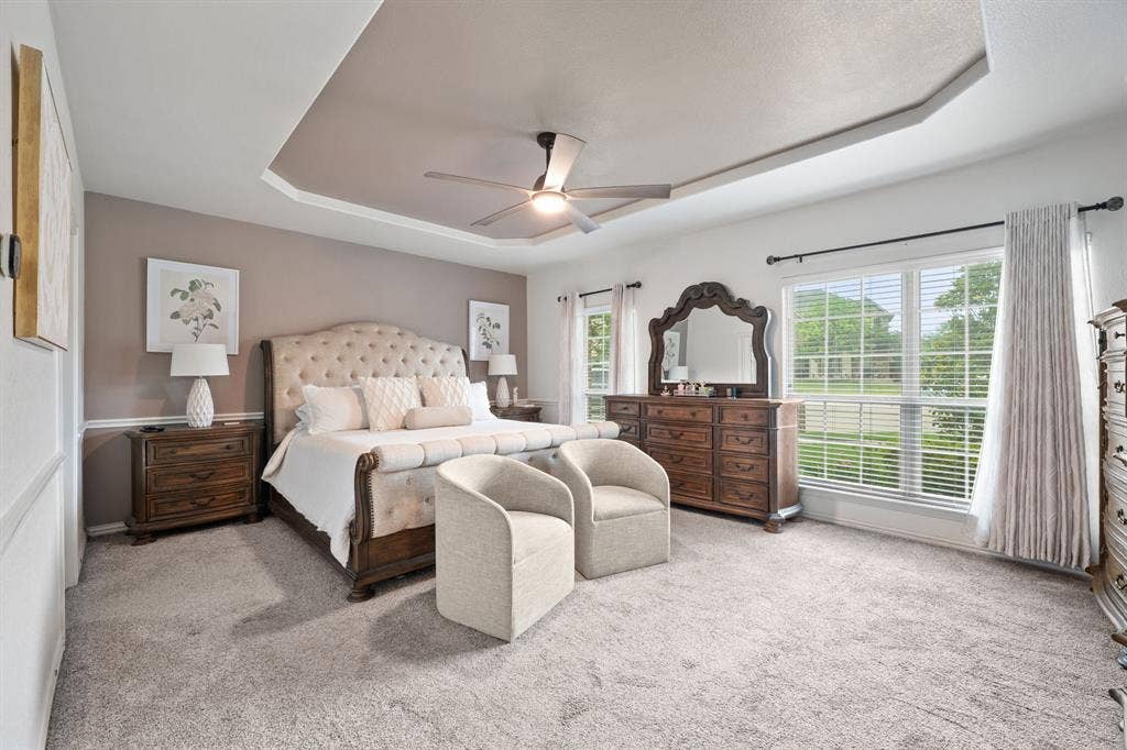 Recessed tray ceiling with crown molding, ceiling fan, and carpeted flooring