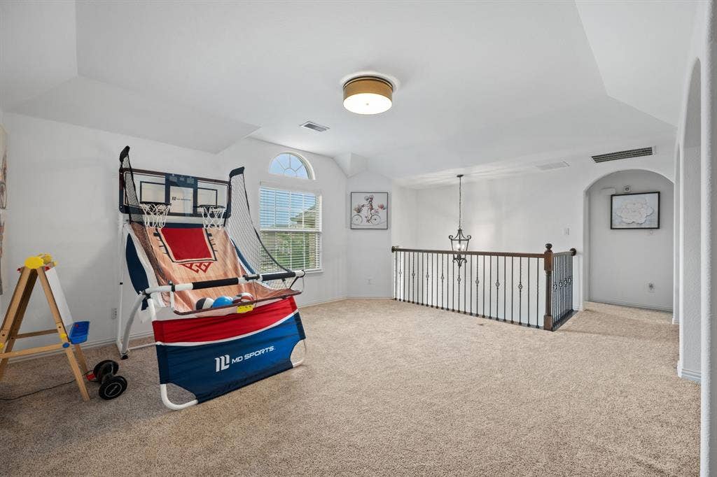 Spacious upper-level game room featuring vaulted ceilings, neutral carpeting, and a juliet balcony