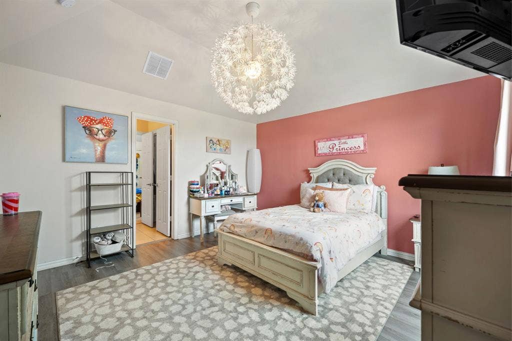 Bedroom featuring a decorative ceiling light fixture, accent wall, wood-finish flooring, and light-toned walls