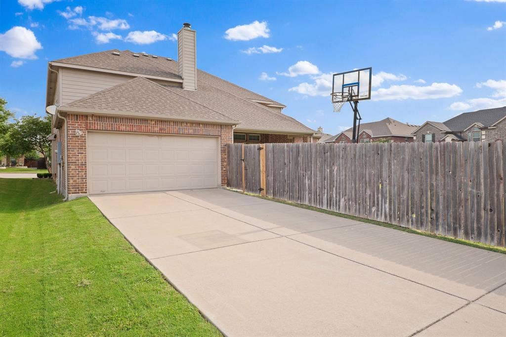 Brick and siding exterior featuring an attached two-car garage with a panel door, a concrete driveway, and a wood fence