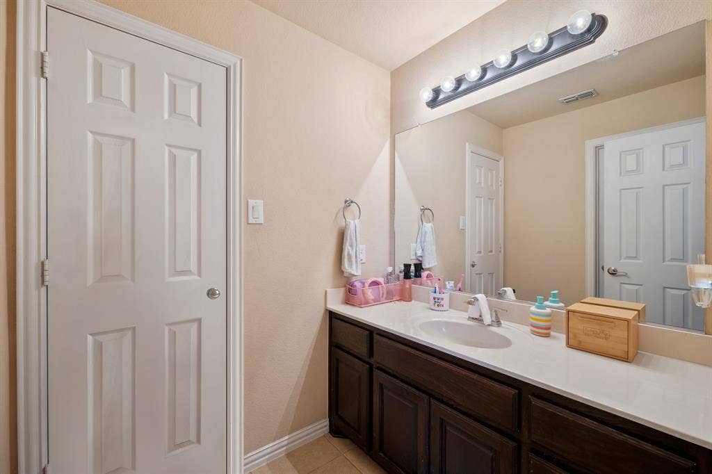 Bathroom vanity featuring a light-toned countertop with an integrated sink, dark wood-finish cabinetry, and a large wall-mounted mirror