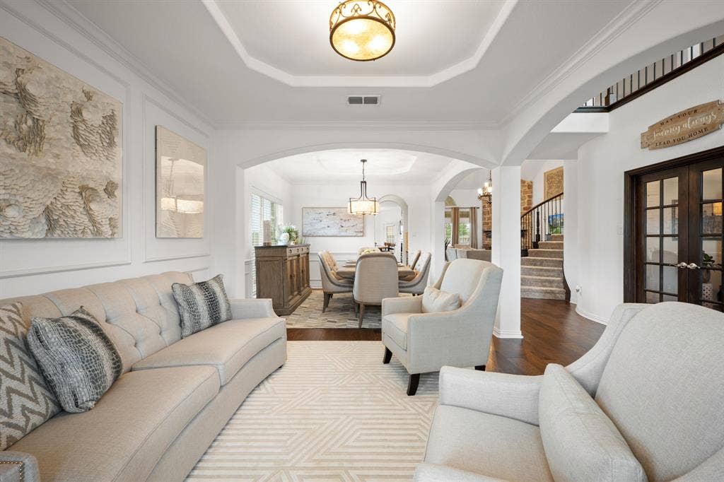 Spacious living area featuring elegant archways, dark wood-finish flooring, and tray ceilings with a semi-flush mount light fixture