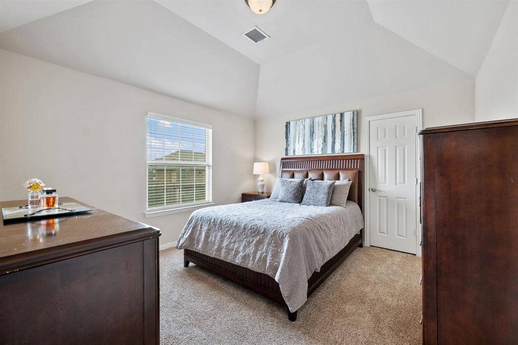 Vaulted ceiling bedroom with a paneled door, window with blinds, and neutral carpeting