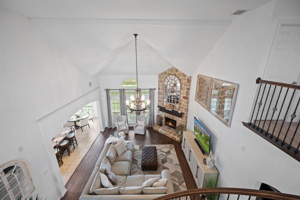 Vaulted great room featuring a stone fireplace with a wood-finish mantle, large windows with arched transoms, and wood-finish flooring