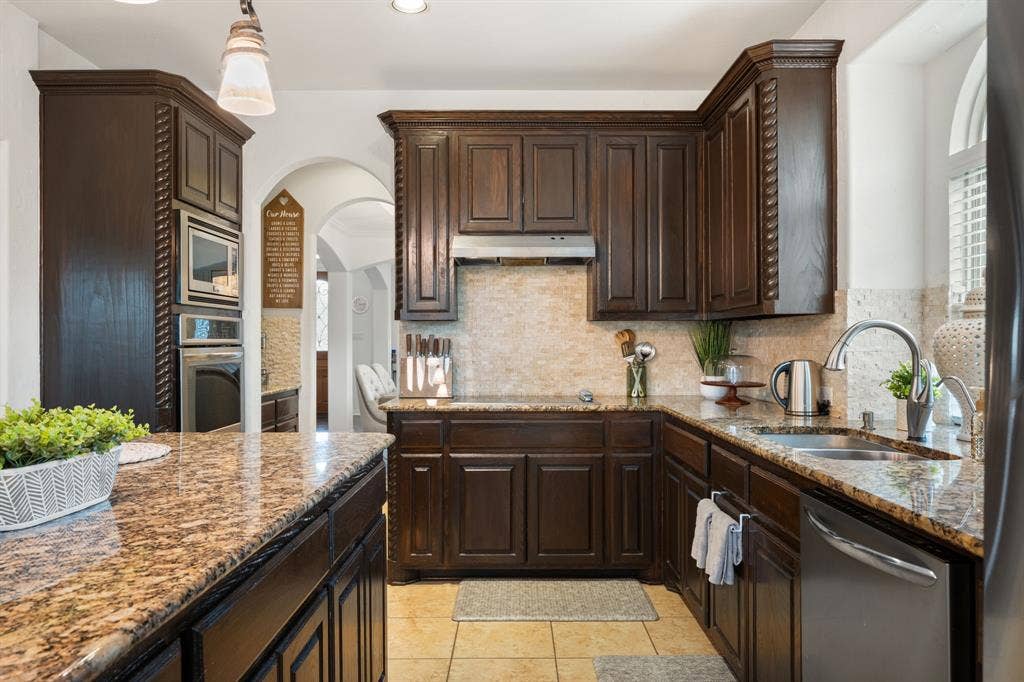 Kitchen featuring dark wood cabinetry, speckled countertops, stainless steel appliances, and stone tile backsplash