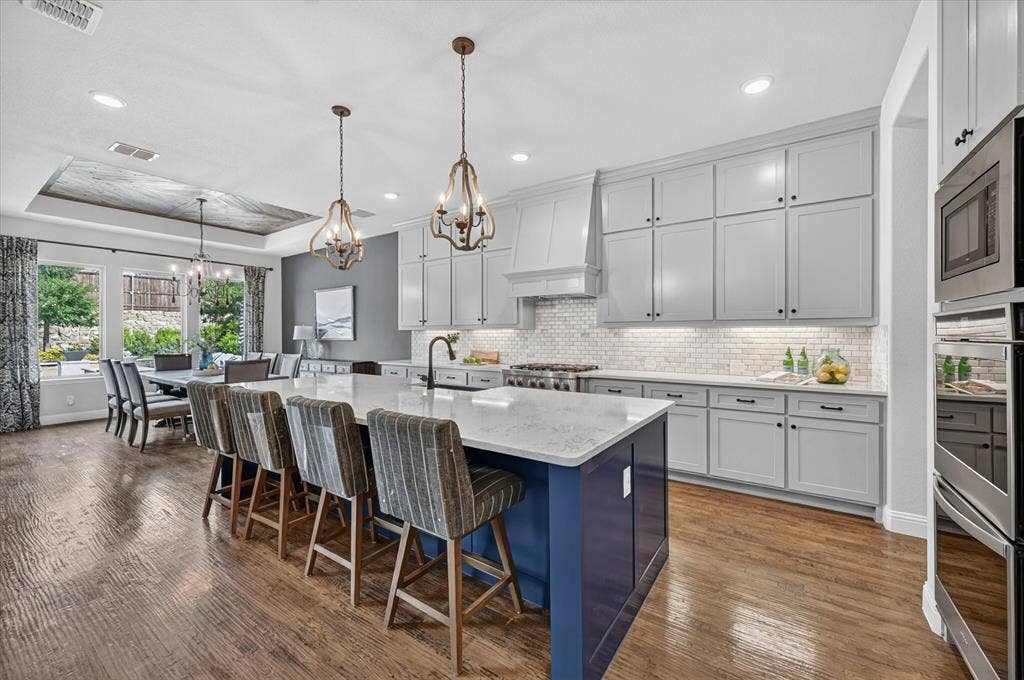 7108 Eagles Ridge Court, Argyle, TX 76226 The chef’s kitchen is equally impressive, offering quartz countertops, a marble backsplash, a six-burner gas rangetop, double ovens, and a large island with breakfast bar seating.