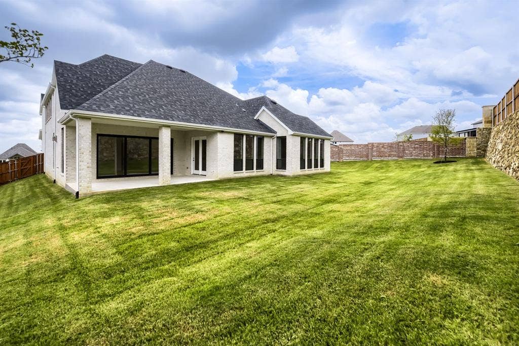794 White Sage Road, Haslet, TX 76052 Expansive rear yard featuring a large covered patio, multiple large windows, a stone retaining wall, and brick fencing