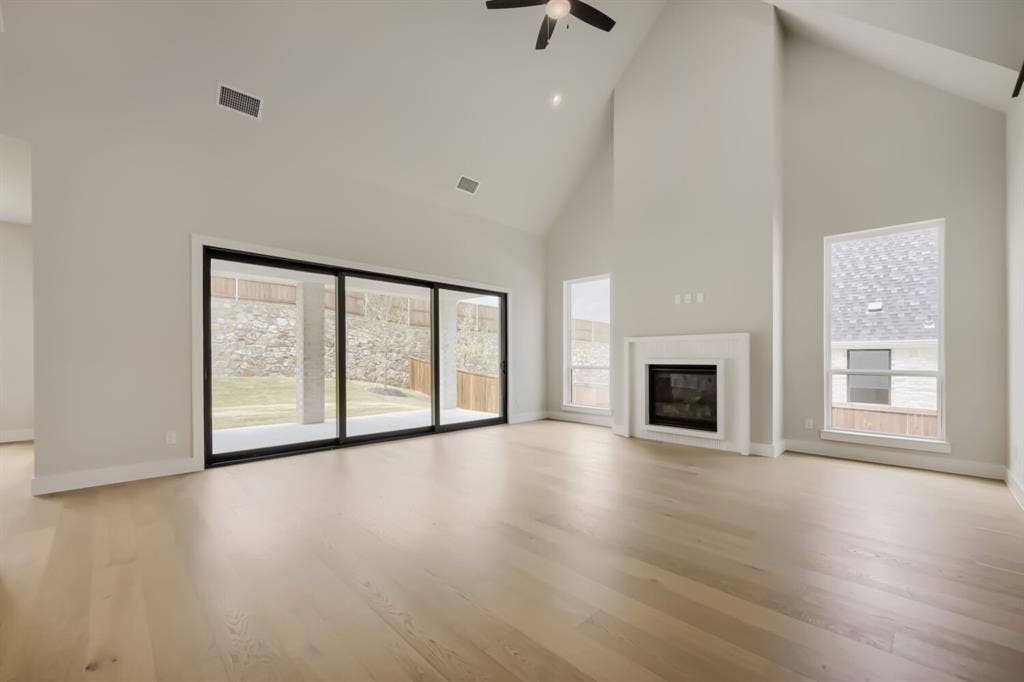 794 White Sage Road, Haslet, TX 76052 Spacious living area featuring a vaulted ceiling with an exposed beam, light wood-finish flooring, a contemporary fireplace with a white surround, and large sliding glass doors opening to the backyard