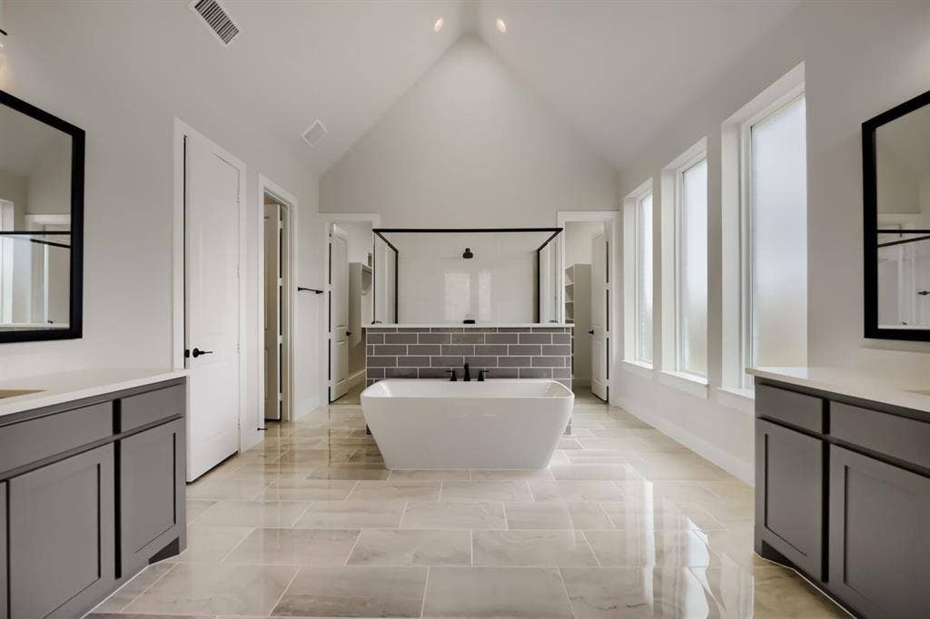 794 White Sage Road, Haslet, TX 76052 Vaulted ceiling bathroom featuring a freestanding tub, gray subway tile shower surround, dual dark gray vanities with integrated sinks, and expansive window array
