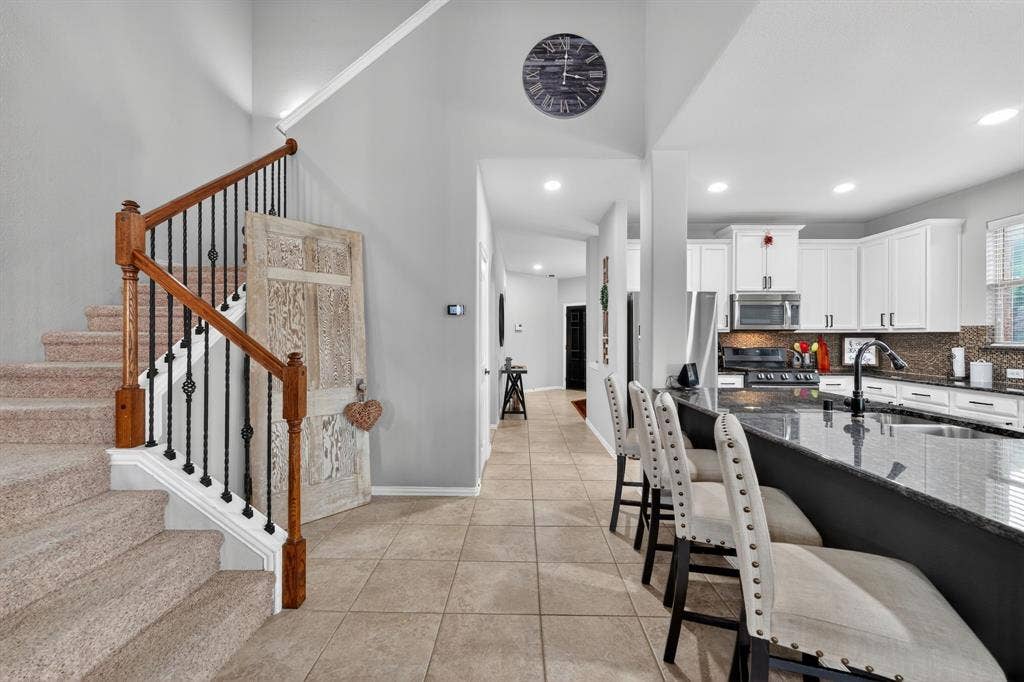 2760 Explorador, Grand Prairie, TX 75054 Carpeted staircase with wood handrails and wrought iron balusters, tile flooring, kitchen with granite countertops, white cabinetry, and stainless steel appliances, recessed lighting throughout
