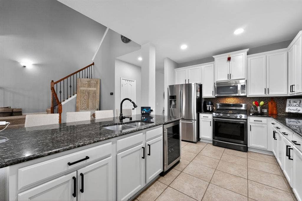 2760 Explorador, Grand Prairie, TX 75054 Kitchen featuring white cabinetry with dark hardware, a center island with an undermount sink, dark countertops, stainless steel appliances, and tiled flooring