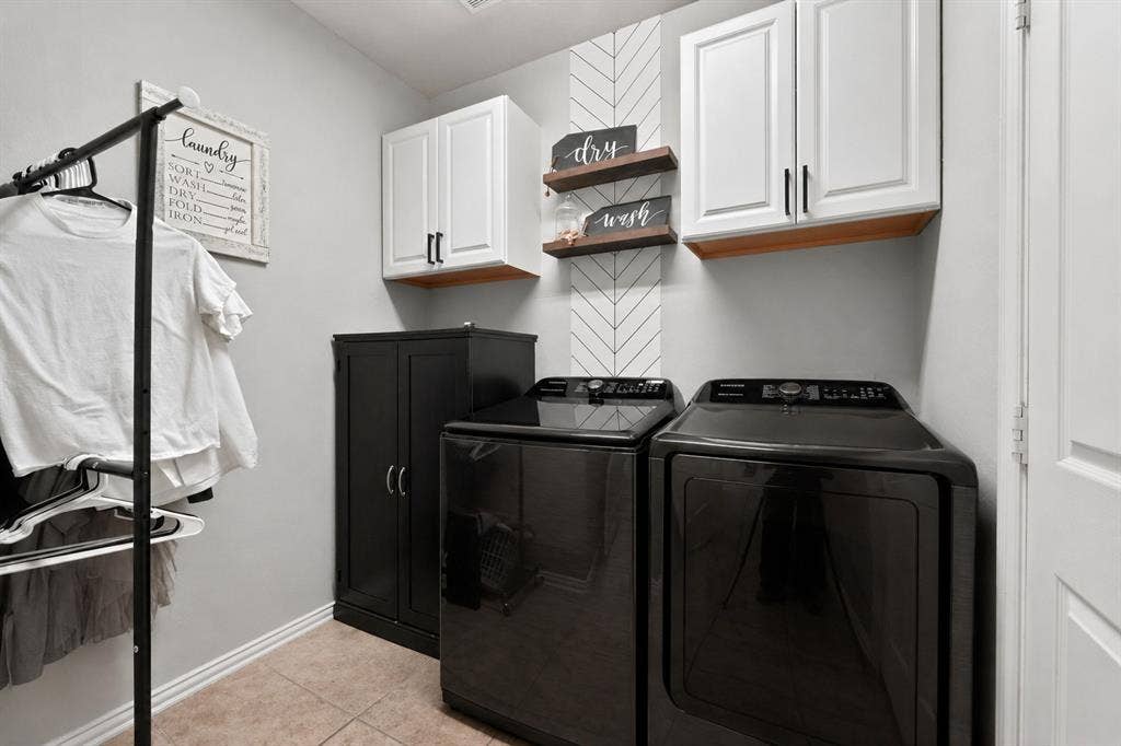 2760 Explorador, Grand Prairie, TX 75054 Laundry area featuring white shaker-style cabinetry with dark pulls, wood-finish shelving, and a patterned accent wall