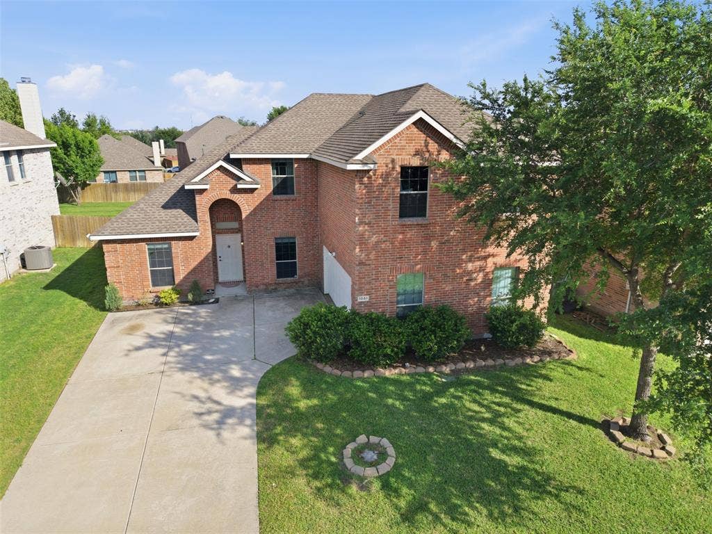 1081 Barrington Drive, Prosper, TX 75078 Brick facade residence featuring an arched entry, mature landscaping, a concrete driveway, and a shingled roof