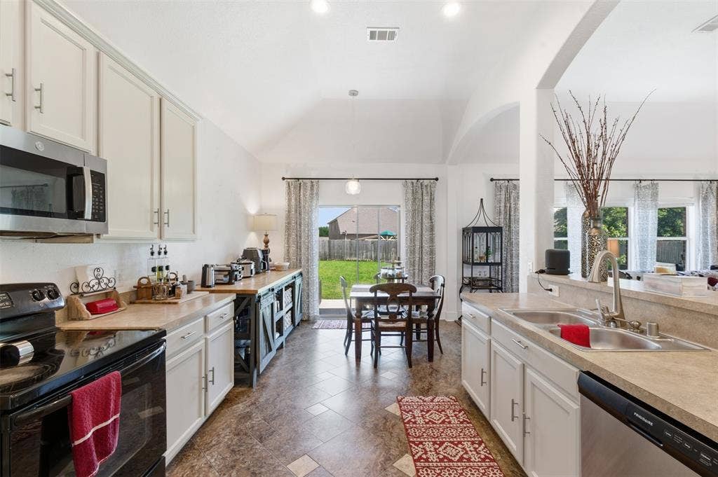 1081 Barrington Drive, Prosper, TX 75078 Open-concept kitchen and dining area featuring vaulted ceilings, white cabinetry, light-toned countertops, and a sliding glass door leading to the backyard