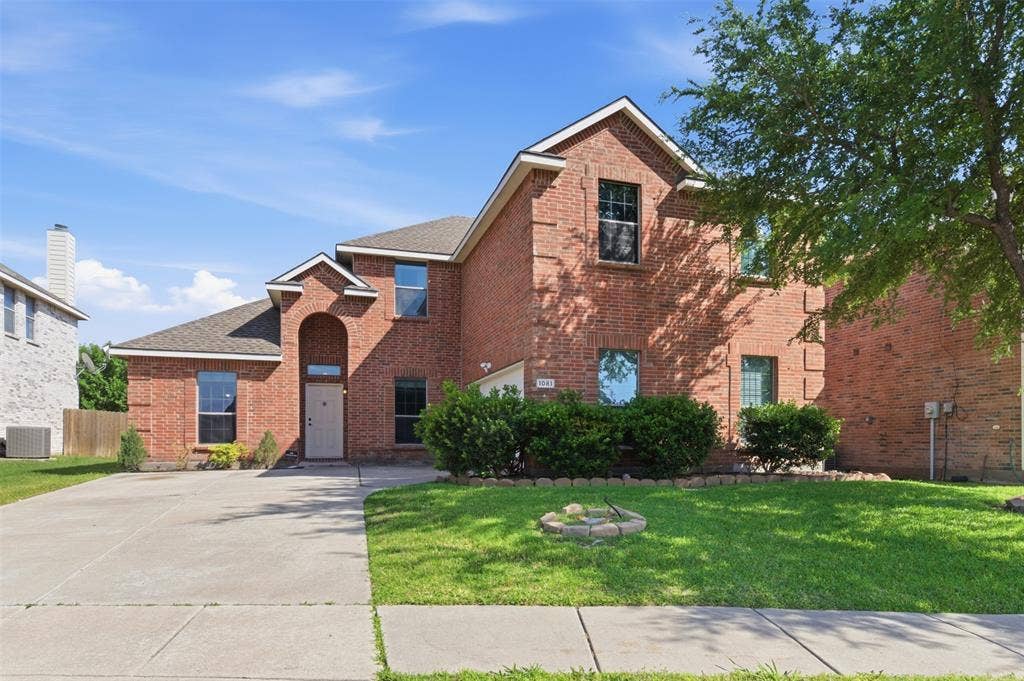 1081 Barrington Drive, Prosper, TX 75078 Brick two-story residence featuring an arched portico entry and a partial front lawn with mature landscaping
