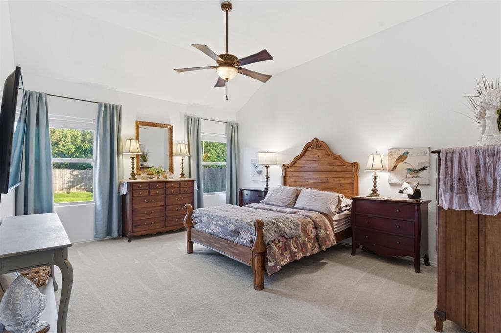 1081 Barrington Drive, Prosper, TX 75078 Vaulted ceiling bedroom featuring plush carpeting, two large windows, and a ceiling fan with integrated lighting