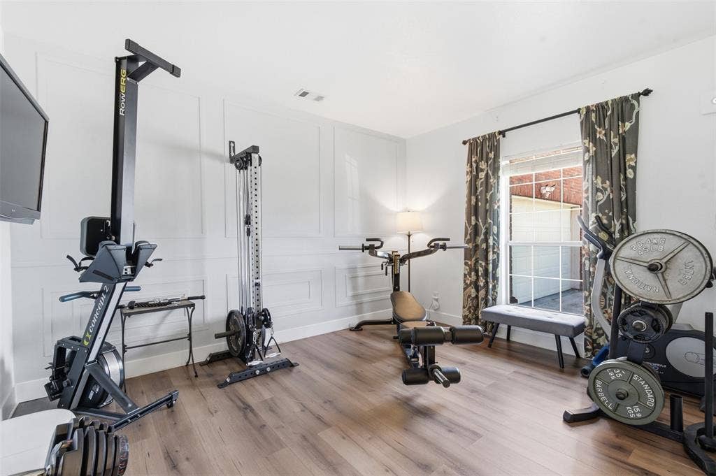 1081 Barrington Drive, Prosper, TX 75078 Room featuring wood-finish flooring, white walls with decorative paneling, and a large window with patterned drapes