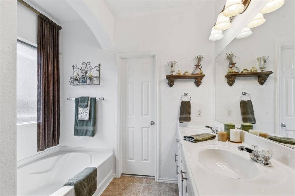 1081 Barrington Drive, Prosper, TX 75078 Bathroom featuring a dual vanity with integrated sinks, a built-in bathtub with a privacy window, and a wall-mounted light fixture